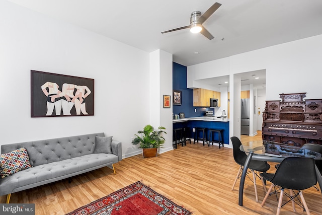 living area featuring light wood-style floors, ceiling fan, and baseboards