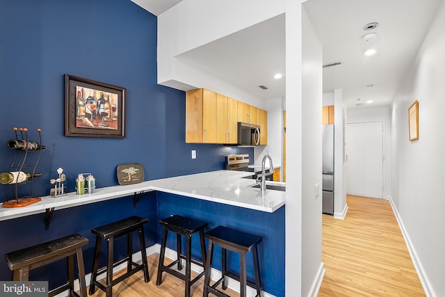 kitchen featuring stainless steel appliances, a kitchen bar, visible vents, light wood-style floors, and baseboards