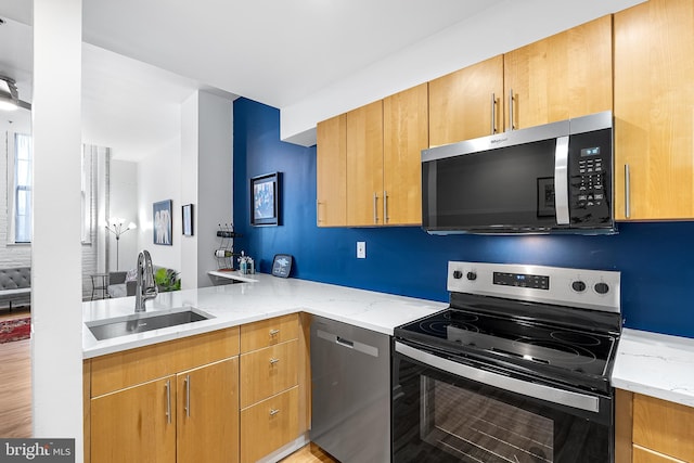 kitchen featuring stainless steel appliances, a sink, a peninsula, and light stone counters