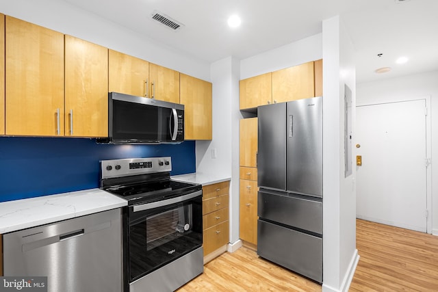 kitchen featuring appliances with stainless steel finishes, light wood-type flooring, visible vents, and light stone countertops