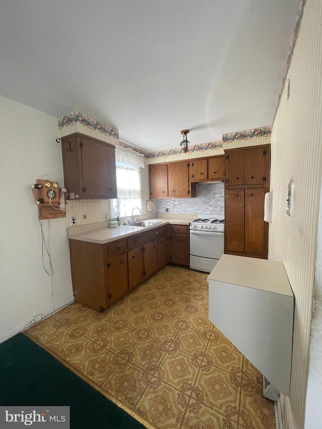 kitchen featuring decorative backsplash, brown cabinets, white gas range, light countertops, and a sink