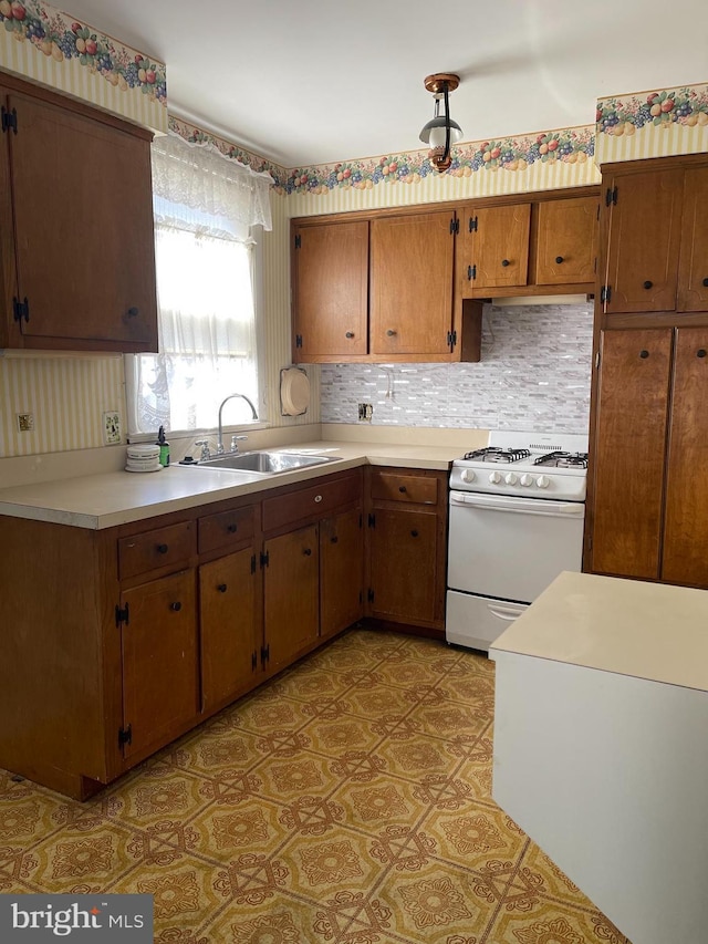 kitchen with a sink, light countertops, brown cabinets, tasteful backsplash, and gas range gas stove