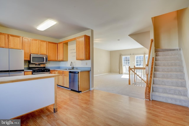 kitchen with stainless steel appliances, light countertops, a sink, and light wood-style flooring