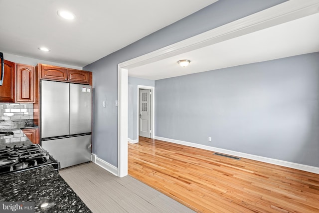 kitchen featuring visible vents, backsplash, baseboards, light wood-style flooring, and freestanding refrigerator