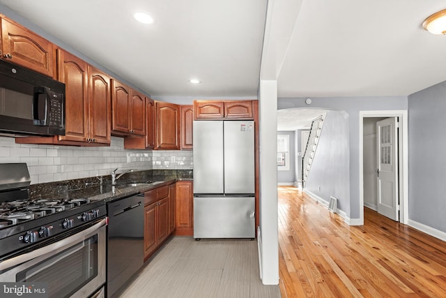 kitchen featuring dark stone countertops, baseboards, a sink, appliances with stainless steel finishes, and tasteful backsplash