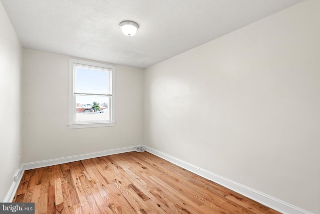 spare room with baseboards, a textured ceiling, and light wood finished floors