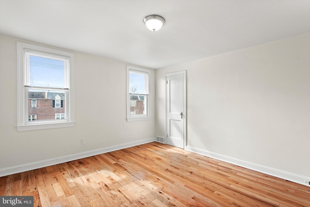 empty room featuring light wood-style flooring, visible vents, and baseboards