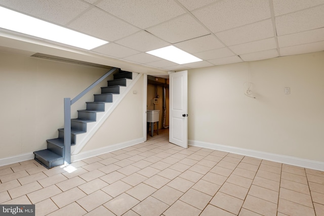 finished below grade area featuring a drop ceiling, stairway, baseboards, and light tile patterned flooring