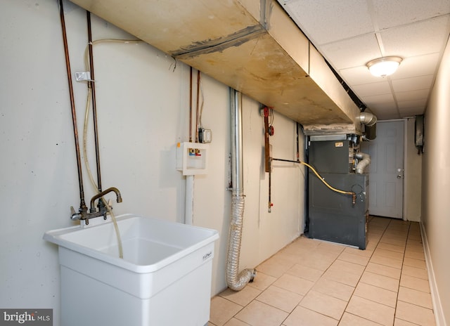 finished below grade area featuring a sink, a drop ceiling, heating unit, and light tile patterned floors