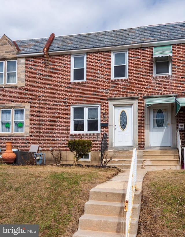 townhome / multi-family property with brick siding, a high end roof, mansard roof, and a front yard