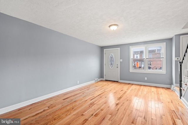 entryway with baseboards, light wood-type flooring, and a textured ceiling