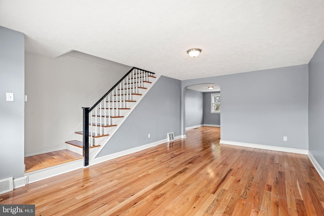 unfurnished living room featuring stairway, arched walkways, baseboards, and hardwood / wood-style floors