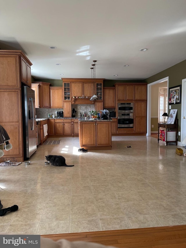 kitchen with a center island, stainless steel appliances, decorative backsplash, brown cabinetry, and glass insert cabinets