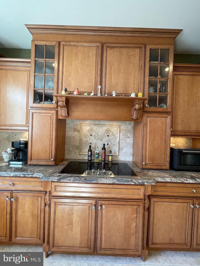 kitchen with dark stone countertops, decorative backsplash, brown cabinetry, and a sink