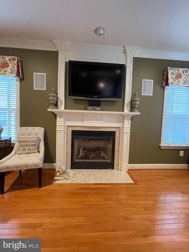 living area with ornamental molding, a fireplace, baseboards, and wood finished floors