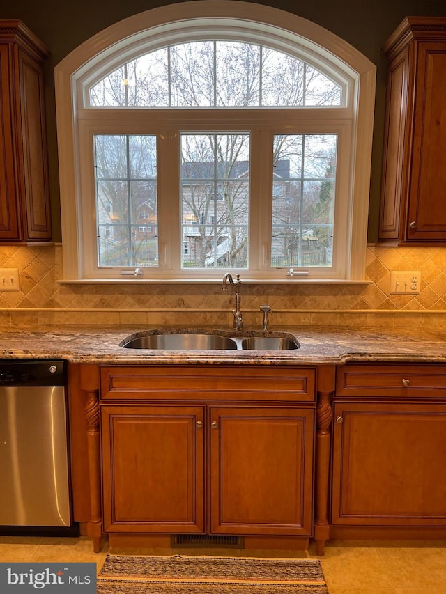 kitchen featuring visible vents, brown cabinets, light stone countertops, stainless steel dishwasher, and a sink