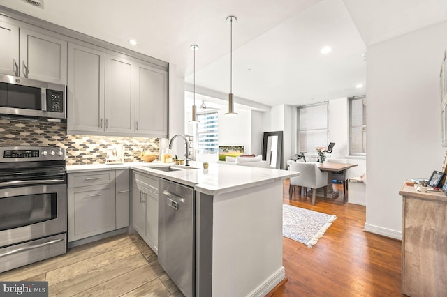 kitchen with a peninsula, gray cabinets, a sink, appliances with stainless steel finishes, and backsplash