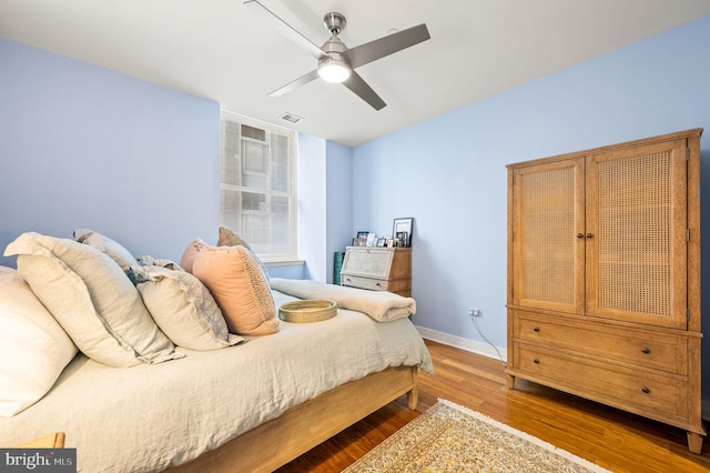 bedroom featuring visible vents, a ceiling fan, baseboards, and wood finished floors