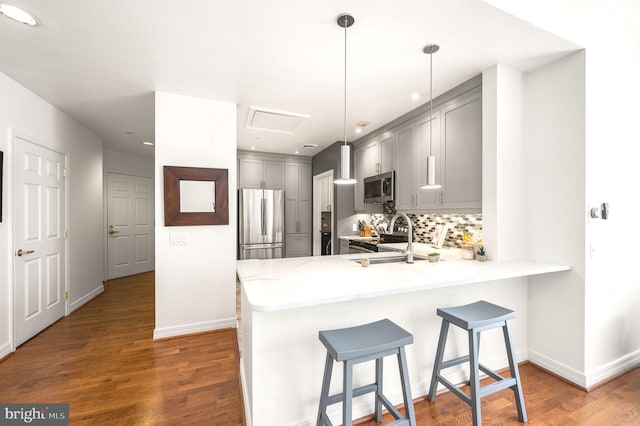 kitchen with gray cabinets, a sink, wood finished floors, a peninsula, and appliances with stainless steel finishes