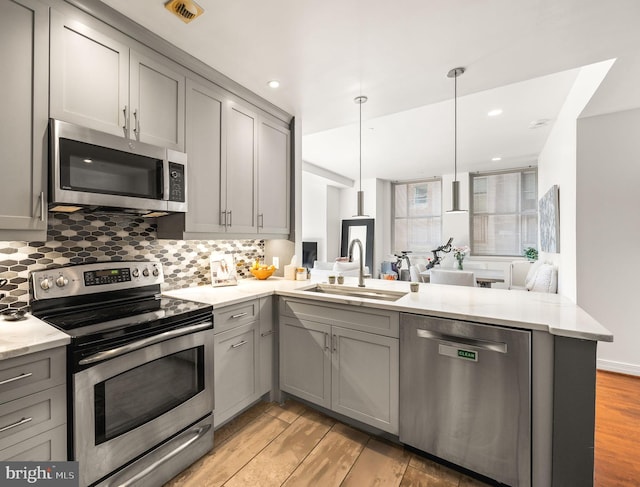 kitchen featuring a peninsula, gray cabinets, a sink, decorative backsplash, and stainless steel appliances