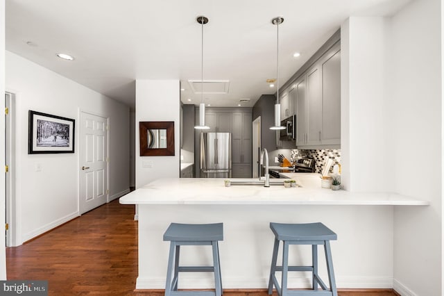 kitchen with dark wood-type flooring, gray cabinetry, a sink, appliances with stainless steel finishes, and a peninsula