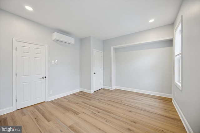 unfurnished room featuring light wood finished floors, a wall mounted air conditioner, and baseboards