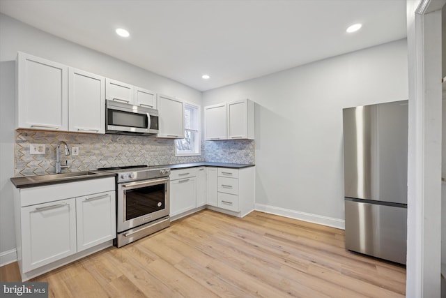 kitchen with dark countertops, backsplash, light wood-style floors, stainless steel appliances, and a sink