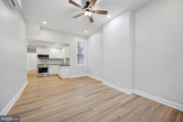 unfurnished living room featuring a wall mounted air conditioner, a sink, recessed lighting, light wood finished floors, and baseboards