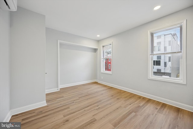 unfurnished room with recessed lighting, baseboards, a wall mounted AC, and light wood-style floors