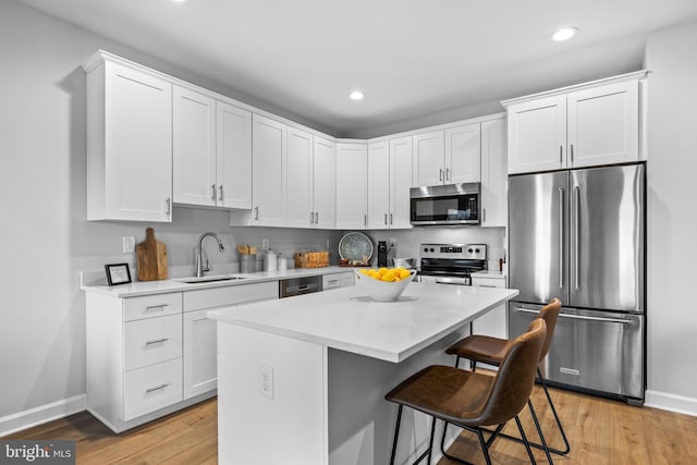 kitchen featuring light wood-style flooring, a breakfast bar, a sink, appliances with stainless steel finishes, and a center island