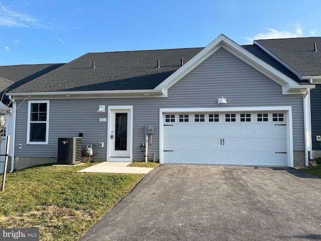 ranch-style house with an attached garage, central air condition unit, aphalt driveway, and roof with shingles