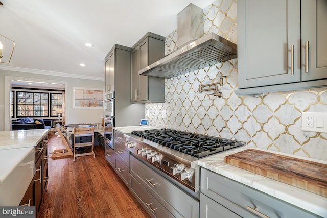 kitchen with wall chimney exhaust hood, appliances with stainless steel finishes, light stone countertops, crown molding, and gray cabinetry