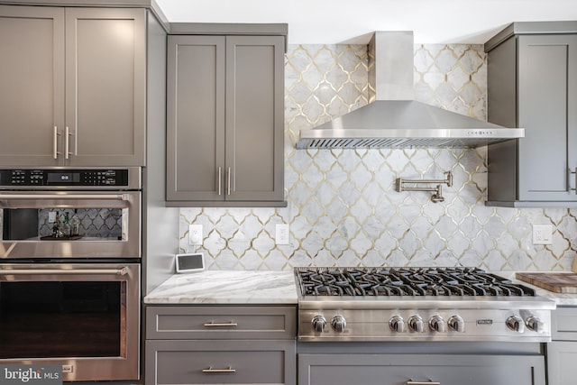 kitchen with appliances with stainless steel finishes, gray cabinets, wall chimney range hood, and decorative backsplash