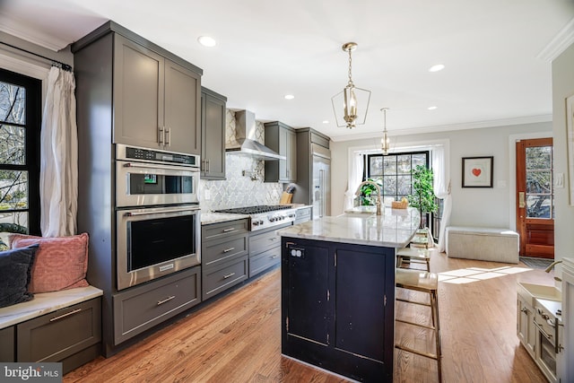 kitchen featuring light wood finished floors, decorative backsplash, appliances with stainless steel finishes, crown molding, and wall chimney range hood