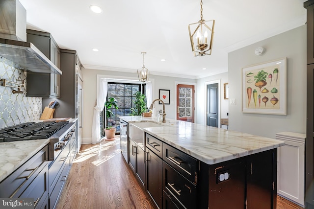 kitchen with appliances with stainless steel finishes, ornamental molding, wood finished floors, wall chimney range hood, and backsplash