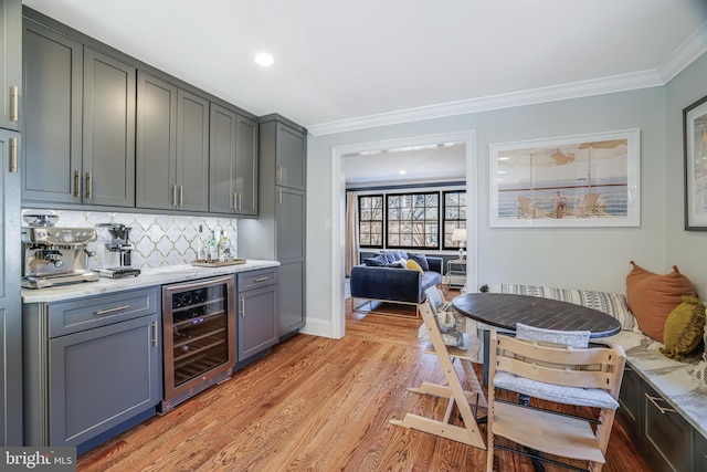 bar featuring crown molding, a dry bar, light wood-style flooring, backsplash, and beverage cooler