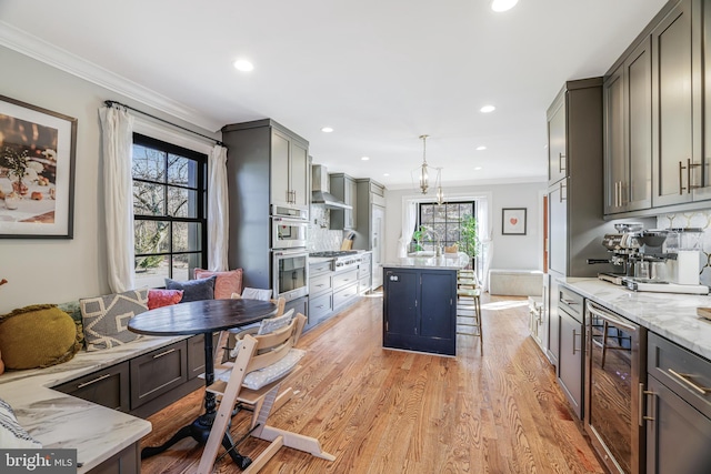 kitchen with beverage cooler, ornamental molding, wall chimney range hood, light wood-type flooring, and breakfast area