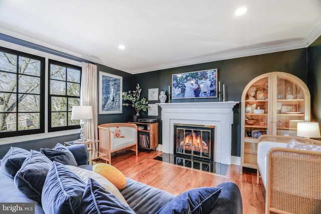 living room featuring a fireplace with flush hearth, ornamental molding, wood finished floors, and recessed lighting