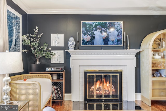 living area featuring baseboards, a fireplace with flush hearth, ornamental molding, and wood finished floors