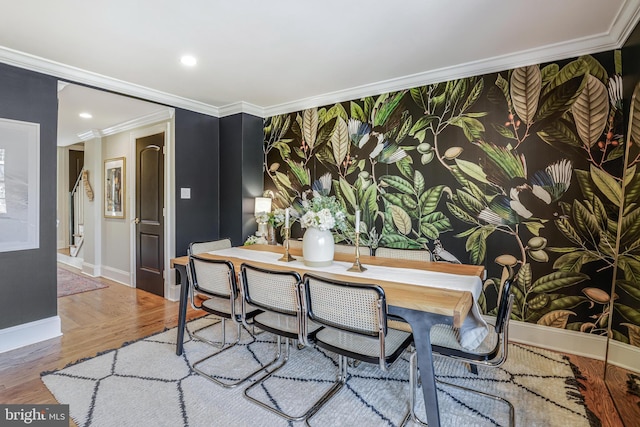 dining area featuring an accent wall, wood finished floors, baseboards, wallpapered walls, and crown molding