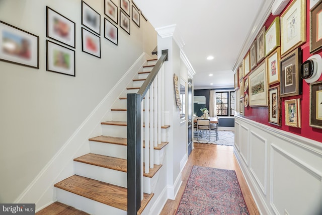 stairway featuring wainscoting, wood finished floors, crown molding, a decorative wall, and recessed lighting