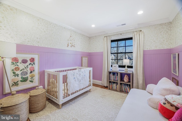 bedroom featuring ornamental molding, a wainscoted wall, visible vents, and wallpapered walls