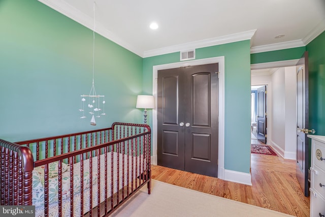 bedroom with crown molding, a closet, visible vents, wood finished floors, and baseboards