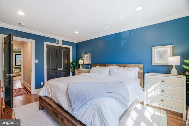 bedroom with baseboards, visible vents, wood finished floors, crown molding, and a closet