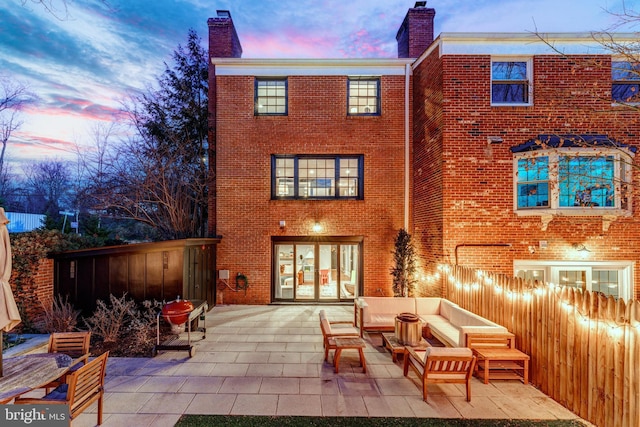 back of house at dusk featuring brick siding, a chimney, a patio area, and an outdoor living space