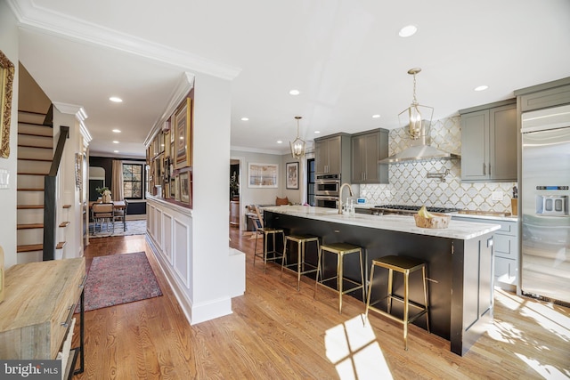 kitchen with light wood-style flooring, gray cabinetry, stainless steel appliances, ornamental molding, and a large island with sink