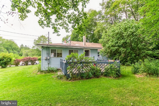 rear view of house featuring a lawn, a chimney, and a wooden deck