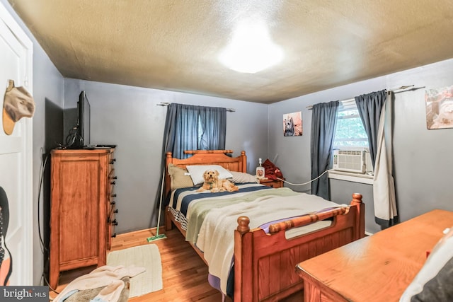 bedroom featuring a textured ceiling, cooling unit, and wood finished floors