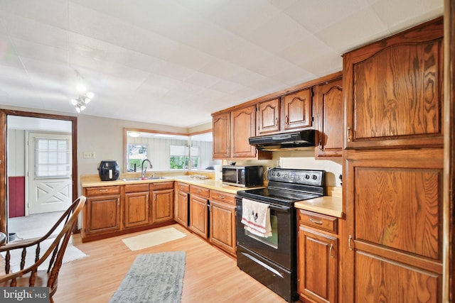 kitchen with black electric range, light countertops, brown cabinetry, a sink, and under cabinet range hood