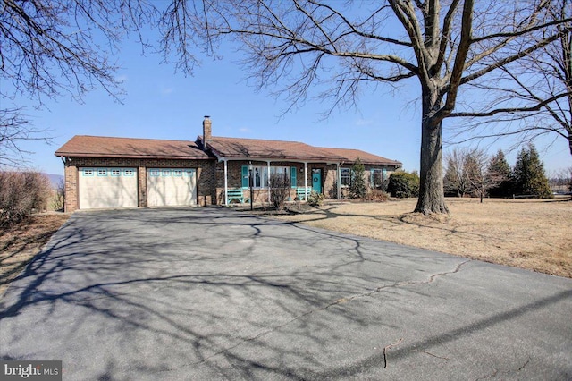 view of front of property with aphalt driveway, a garage, covered porch, brick siding, and a chimney